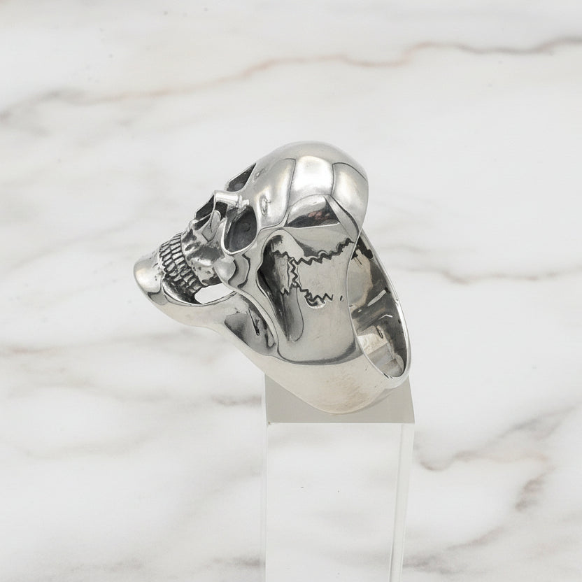 Silver skull-shaped ring on a white stand with a white background