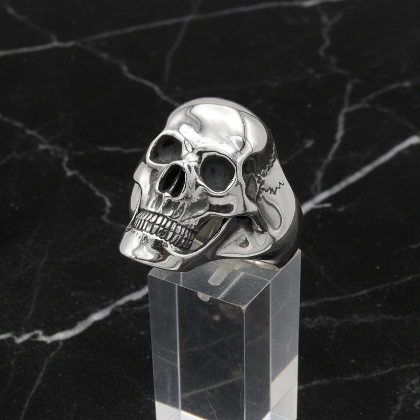 Silver skull ring on a clear stand with a black marble background