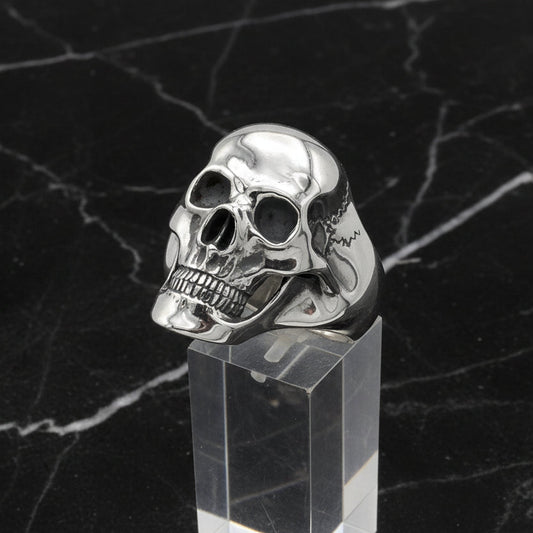 Silver skull ring on a clear stand with a black marble background