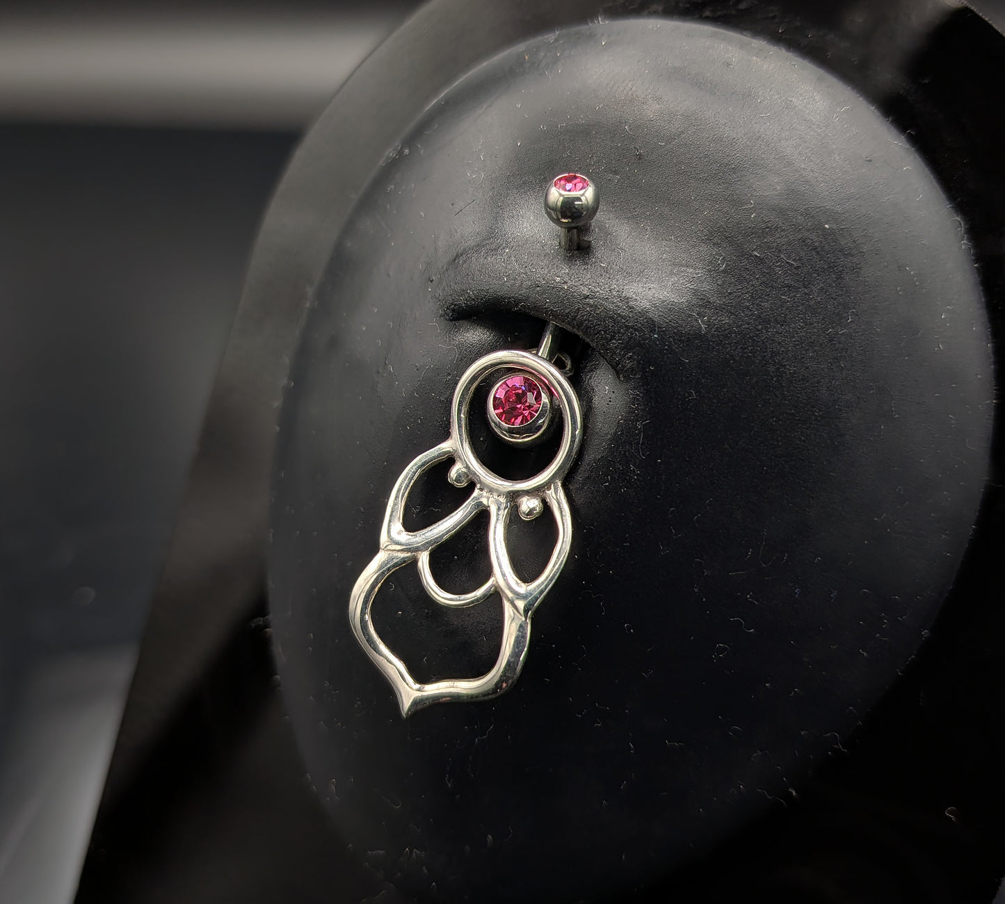 Silver mandala style navel shield with a jewelled barbell on a dark background