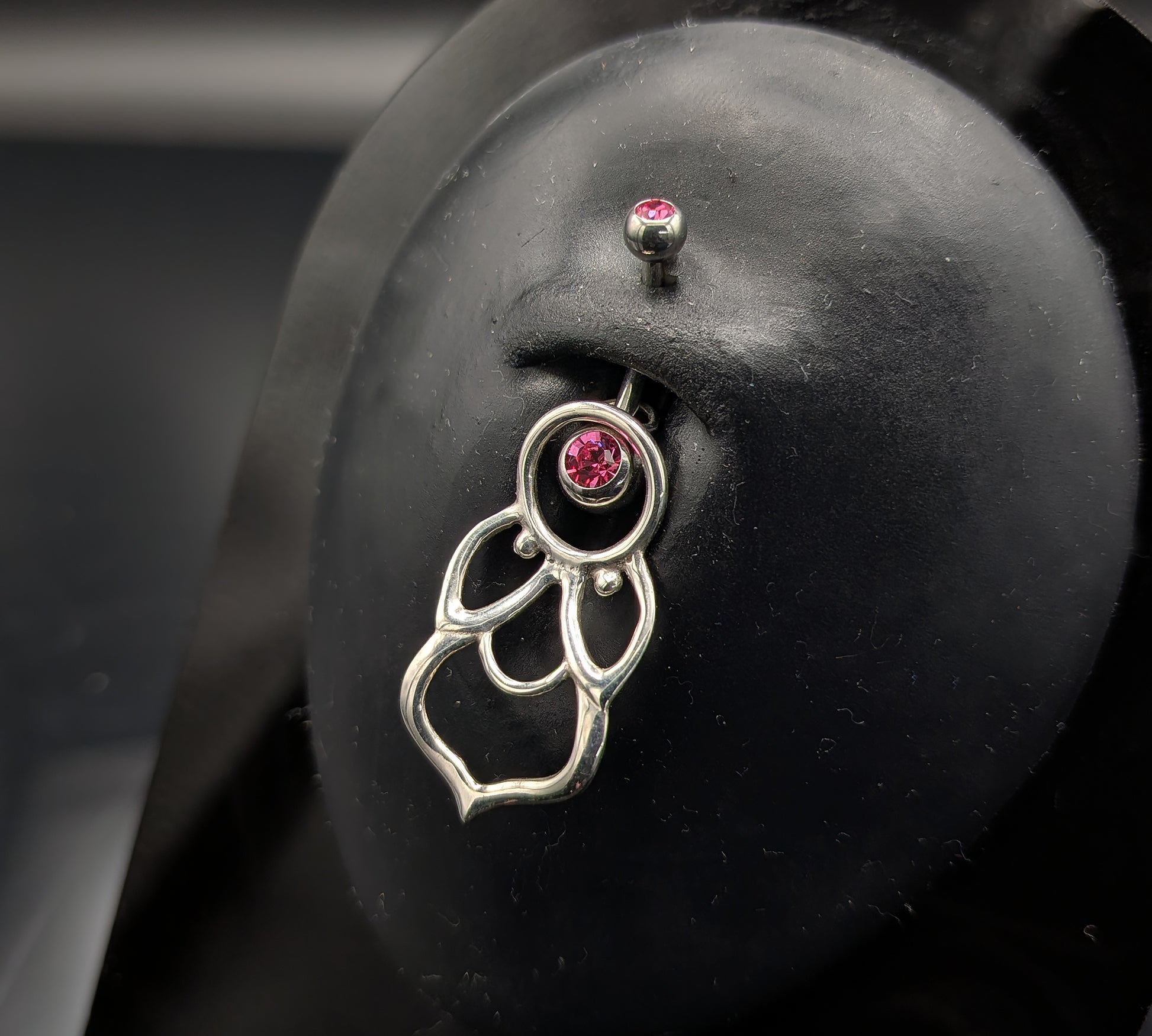 Silver mandala style navel shield with a jewelled barbell on a dark background