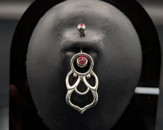 Silver mandala style navel shield with a jewelled barbell on a dark background