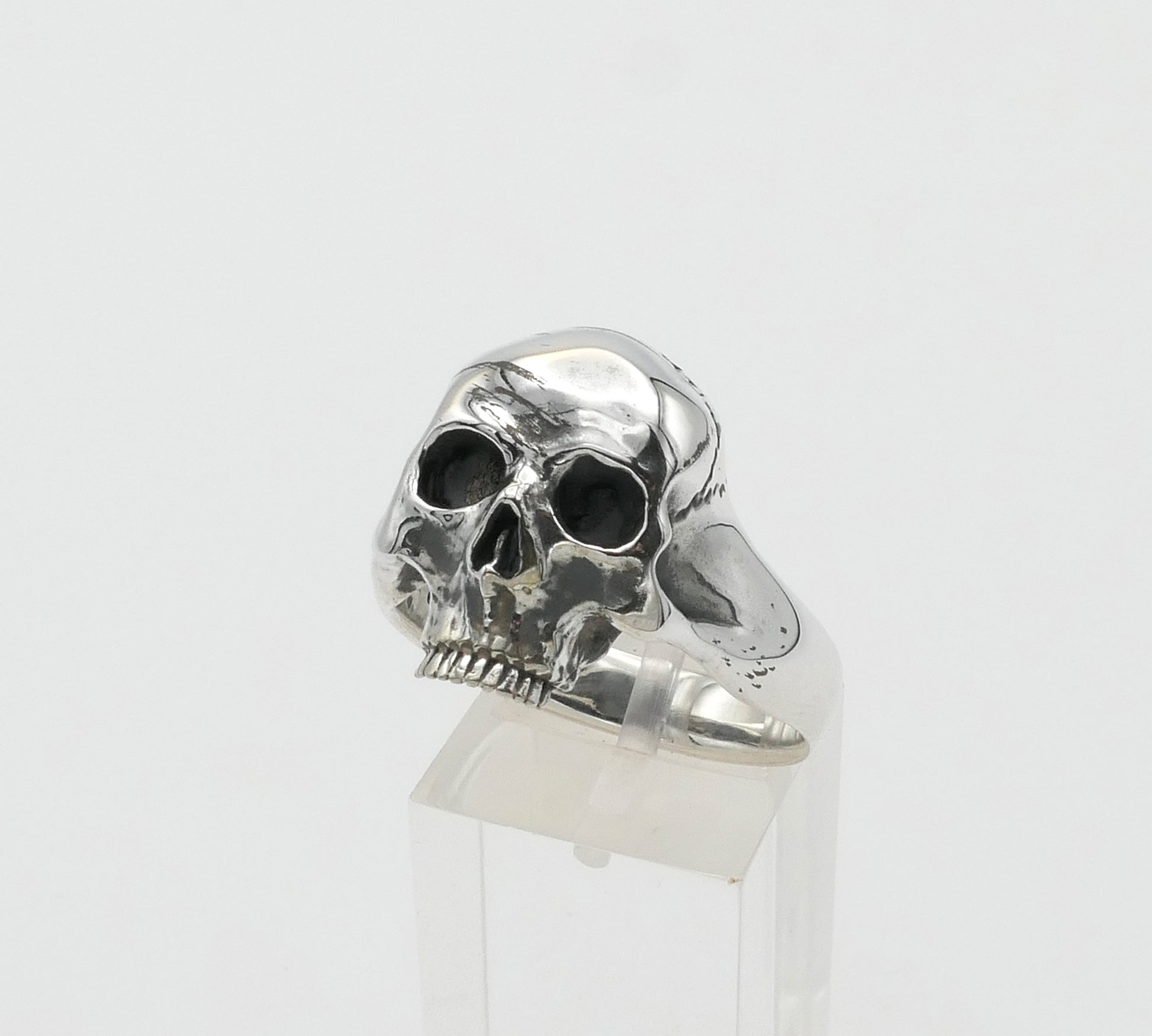 Silver skull ring on a clear stand against a white background