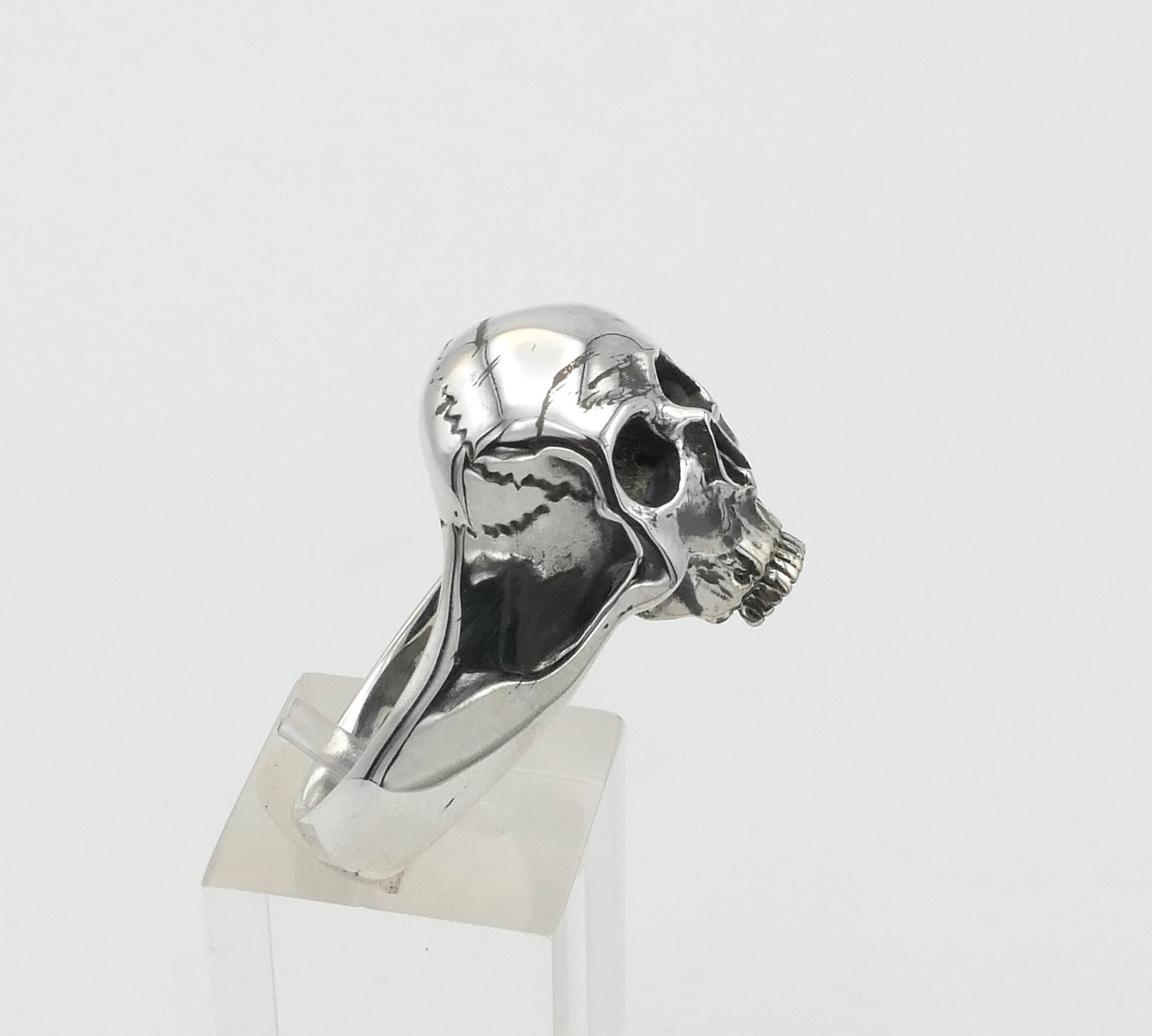 Silver skull-shaped ring on a clear stand against a white background