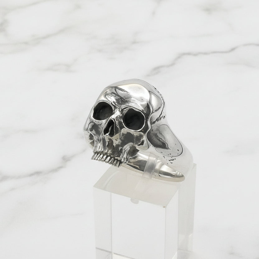 Silver skull ring on a clear stand against a white background