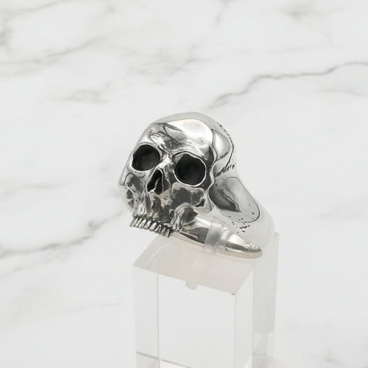 Silver skull ring on a clear stand against a white background