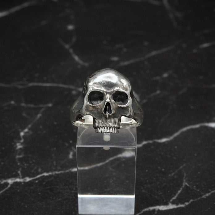 A sterling silver skull ring displayed in a clear case, with a polished finish and no lower jaw.
