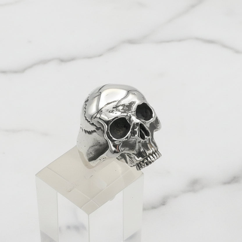 Silver skull ring on a clear stand with a white background