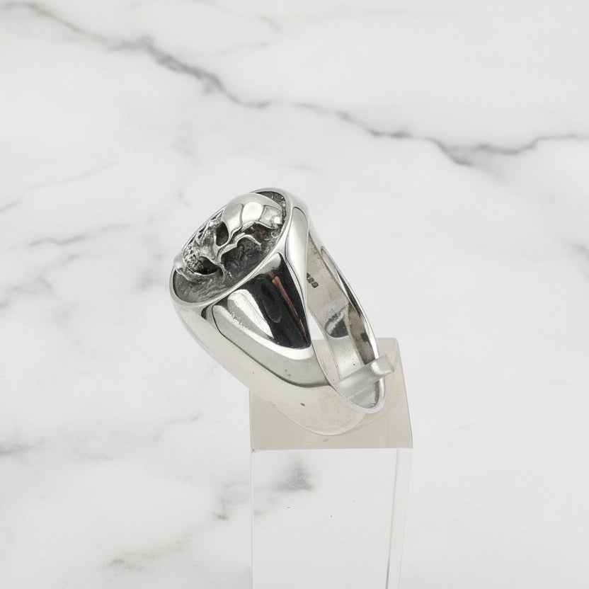 Silver signet ring on a clear stand against a white background
