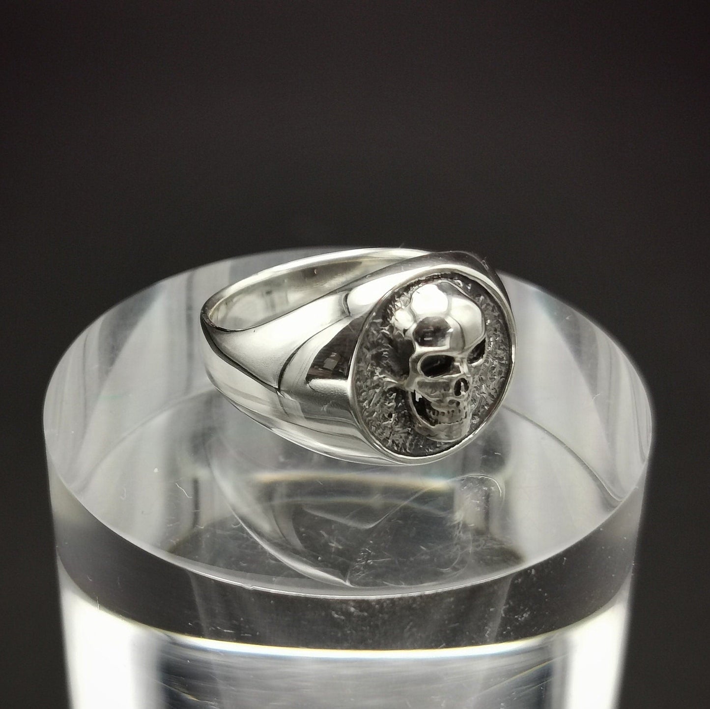 Silver ring with skull design on a clear stand against a black background