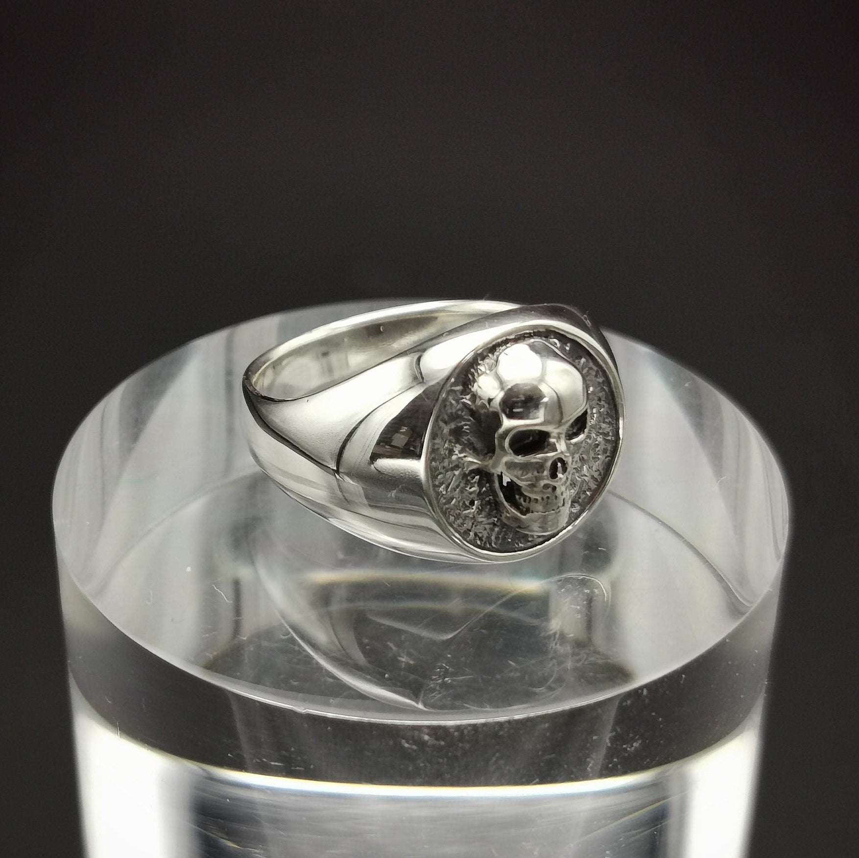 Silver ring with skull design on a clear stand against a black background