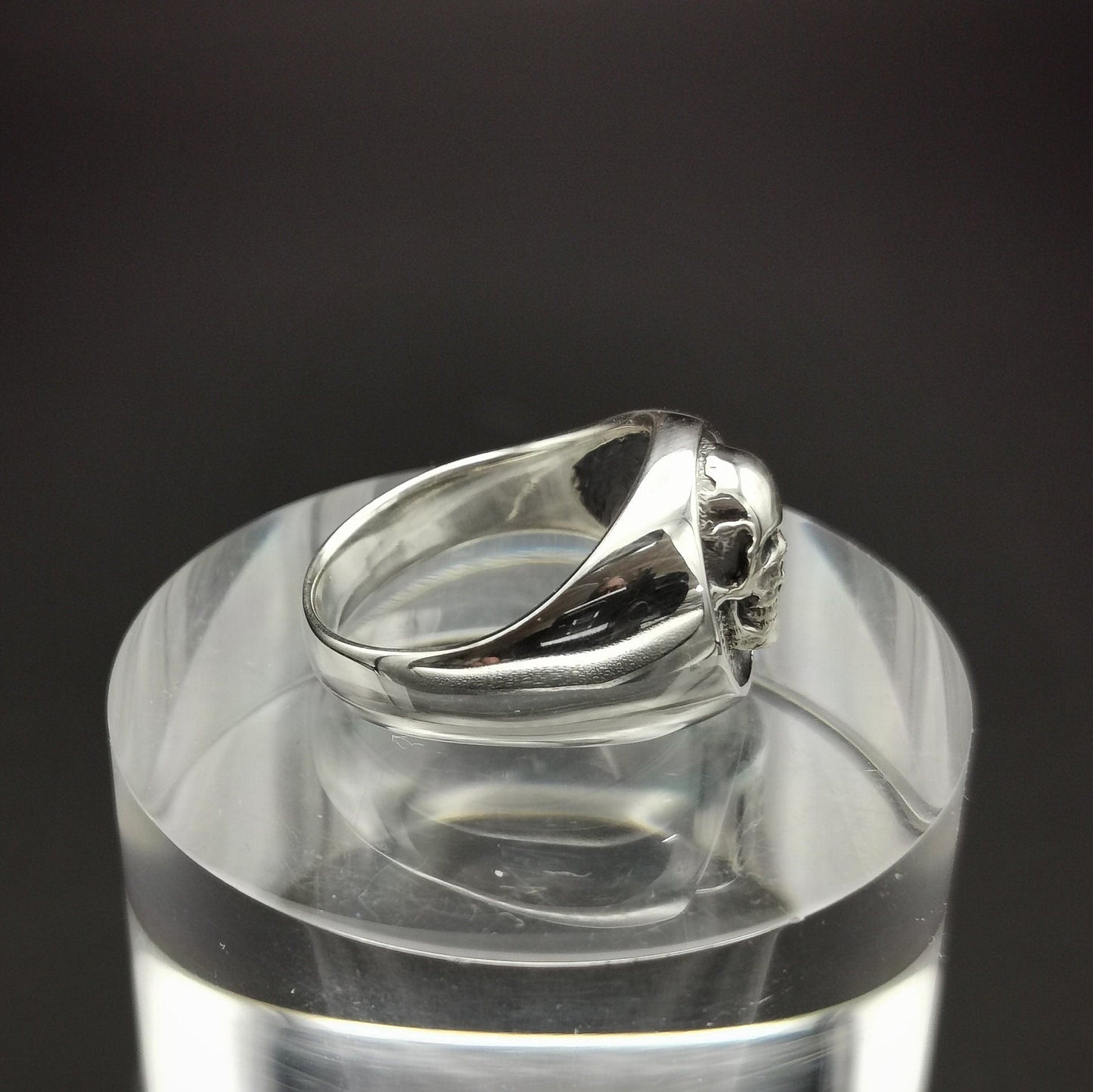 Silver ring on a clear cylindrical stand with a black background