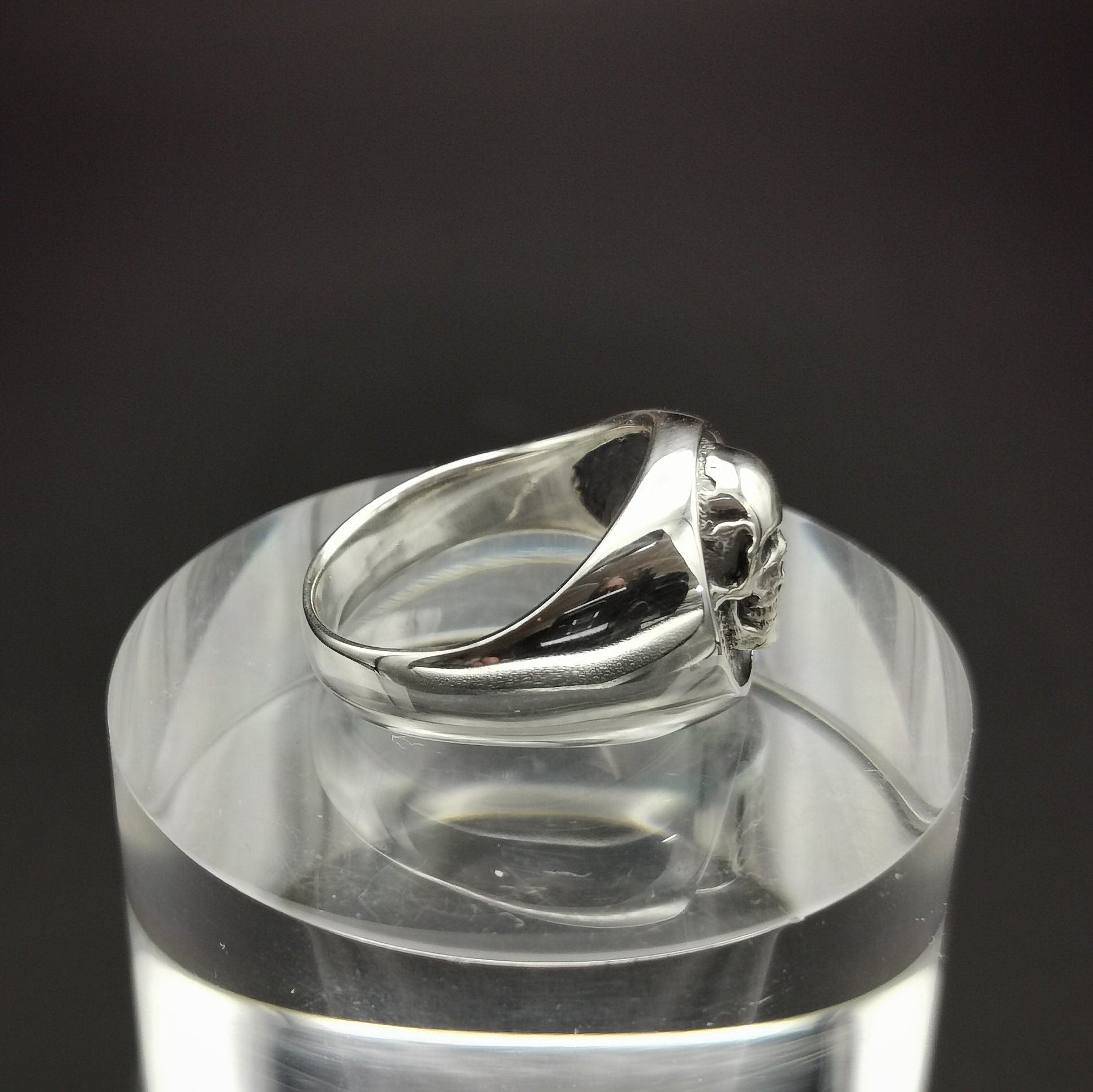 Silver ring on a clear cylindrical stand with a black background