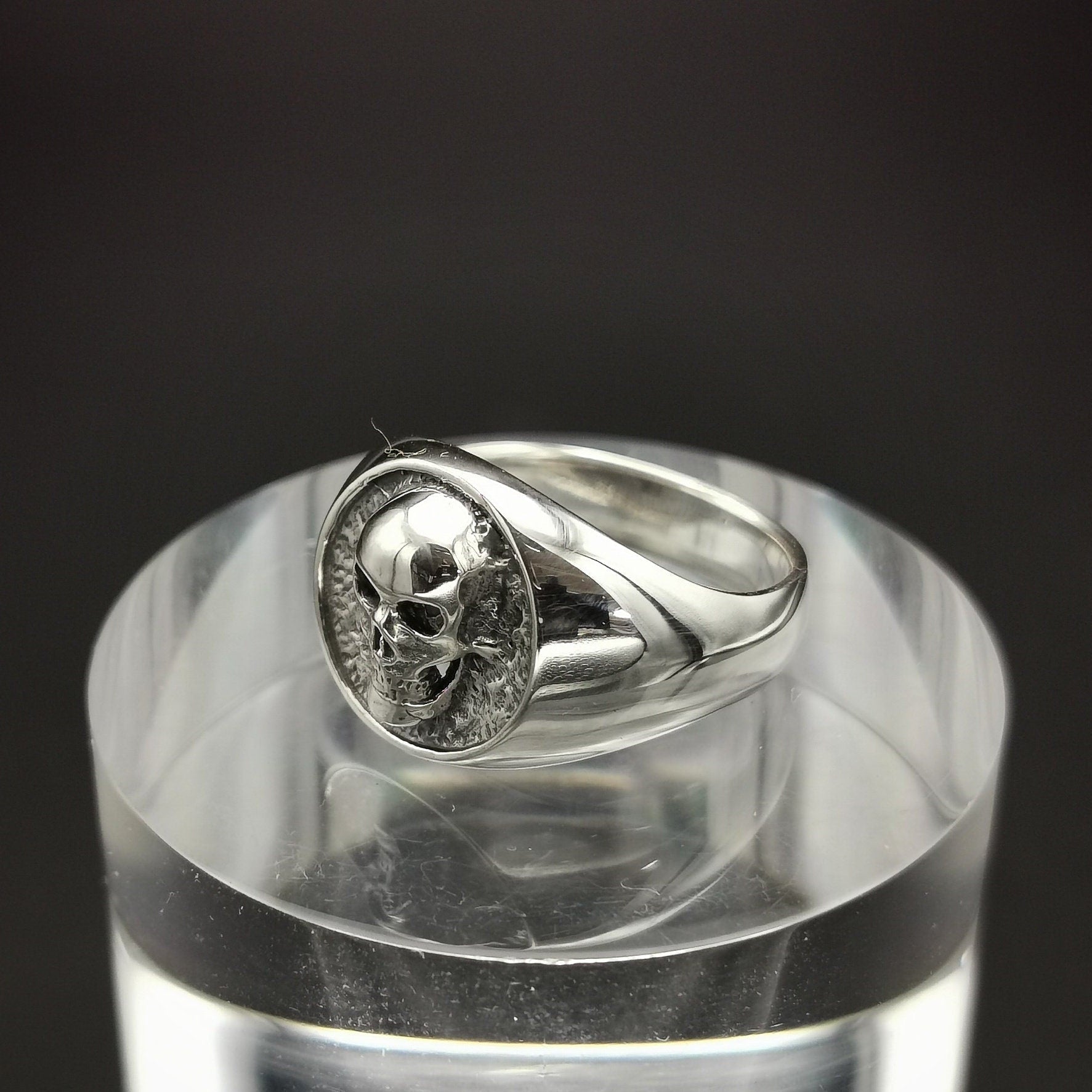 Silver skull ring on a clear stand with a black background