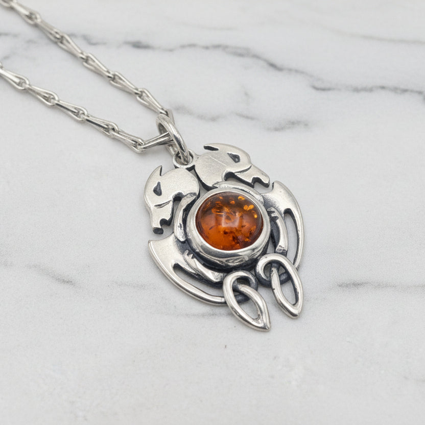 Silver pendant with a central amber stone on a light gray background