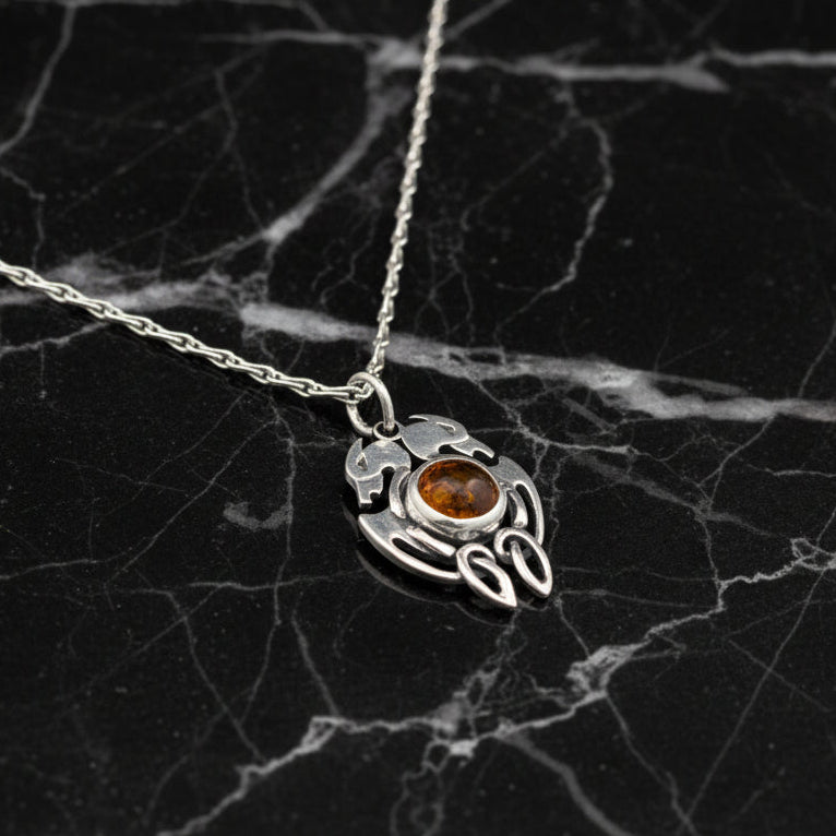 Silver necklace with a pendant featuring an orange gemstone on a black background