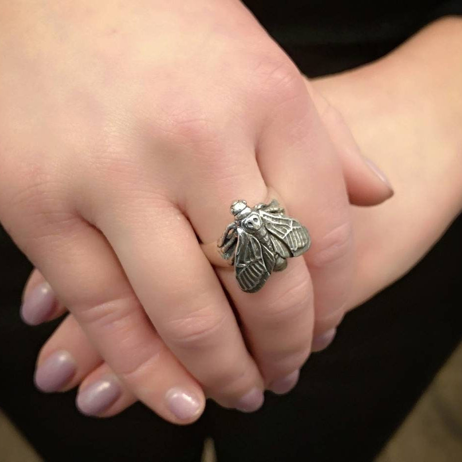 Silver hawk moth ring on a person's finger with a blurred background