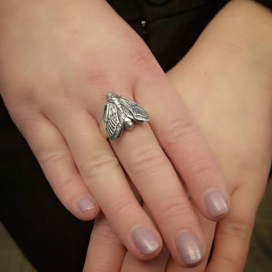 Silverhawk moth ring on a person's finger with a blurred background