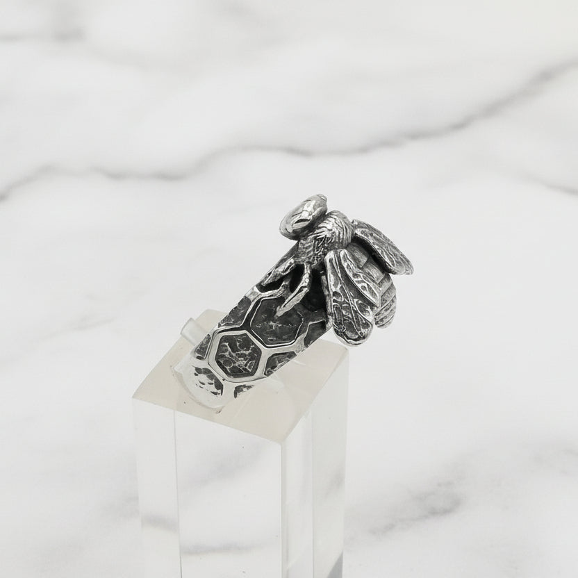 Silver bee ring on a clear stand against a white background