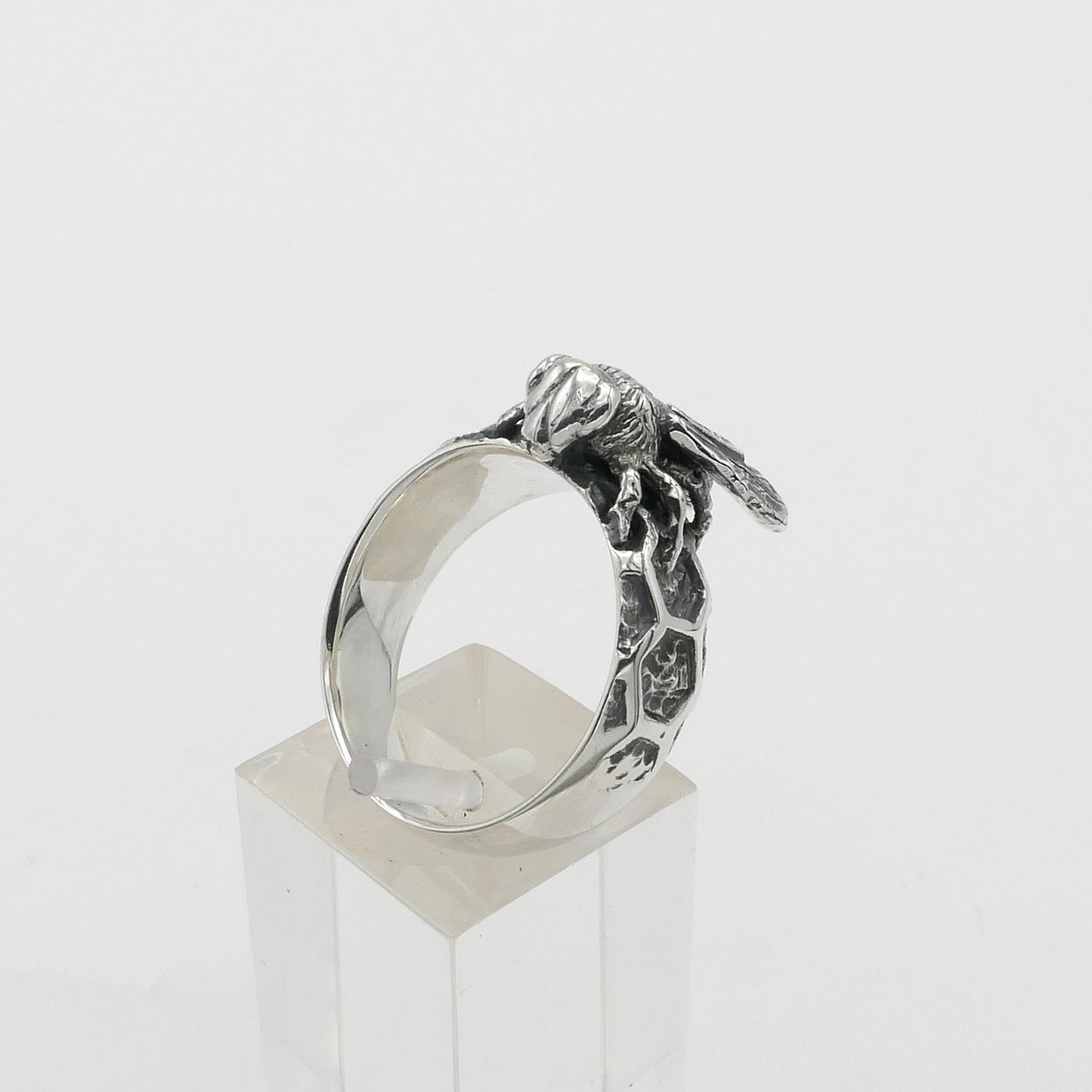 Silver ring with a detailed design on a clear stand against a white background