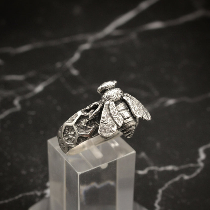 Silver bee-shaped ring on a clear stand against a black background