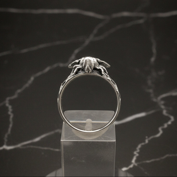 Silver ring with a detailed design on a clear stand against a dark marble background