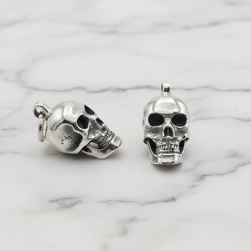 Pair of silver skull-shaped earrings on a light gray background