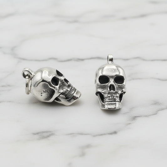 Pair of silver skull-shaped earrings on a light gray background