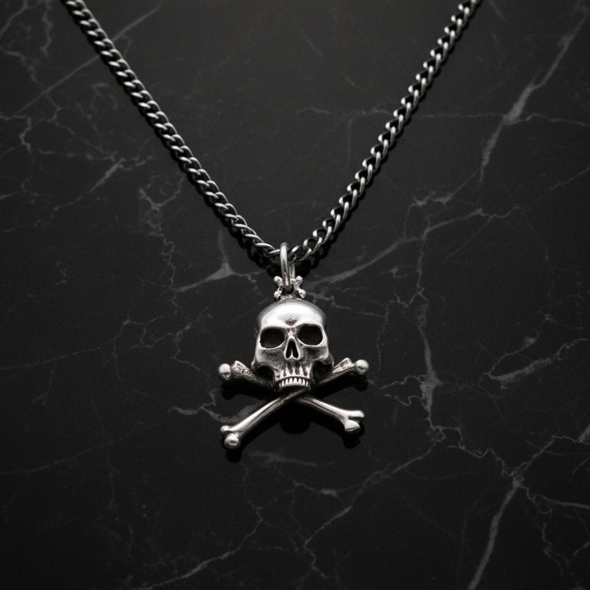 Sterling silver skull and crossbones pendant necklace with a heavy curb chain displayed on a black marble background.