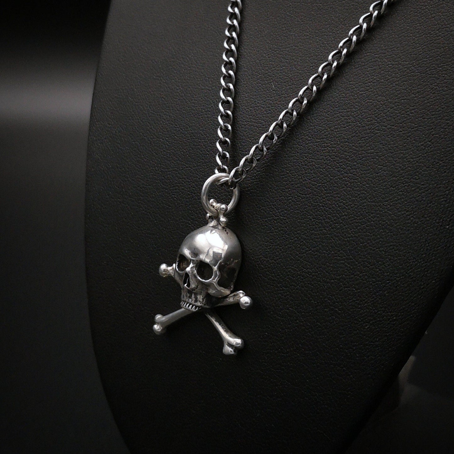 Silver skull and crossbones pendant on a chain against a dark background
