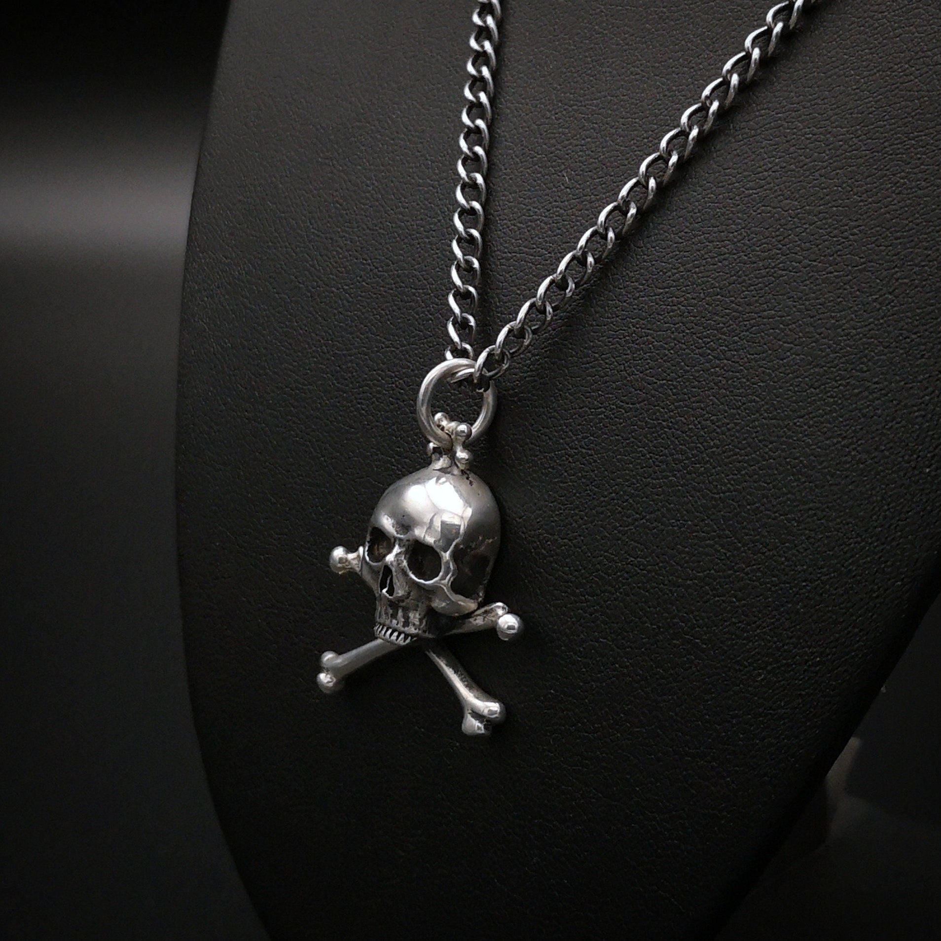Silver skull and crossbones pendant on a chain against a dark background