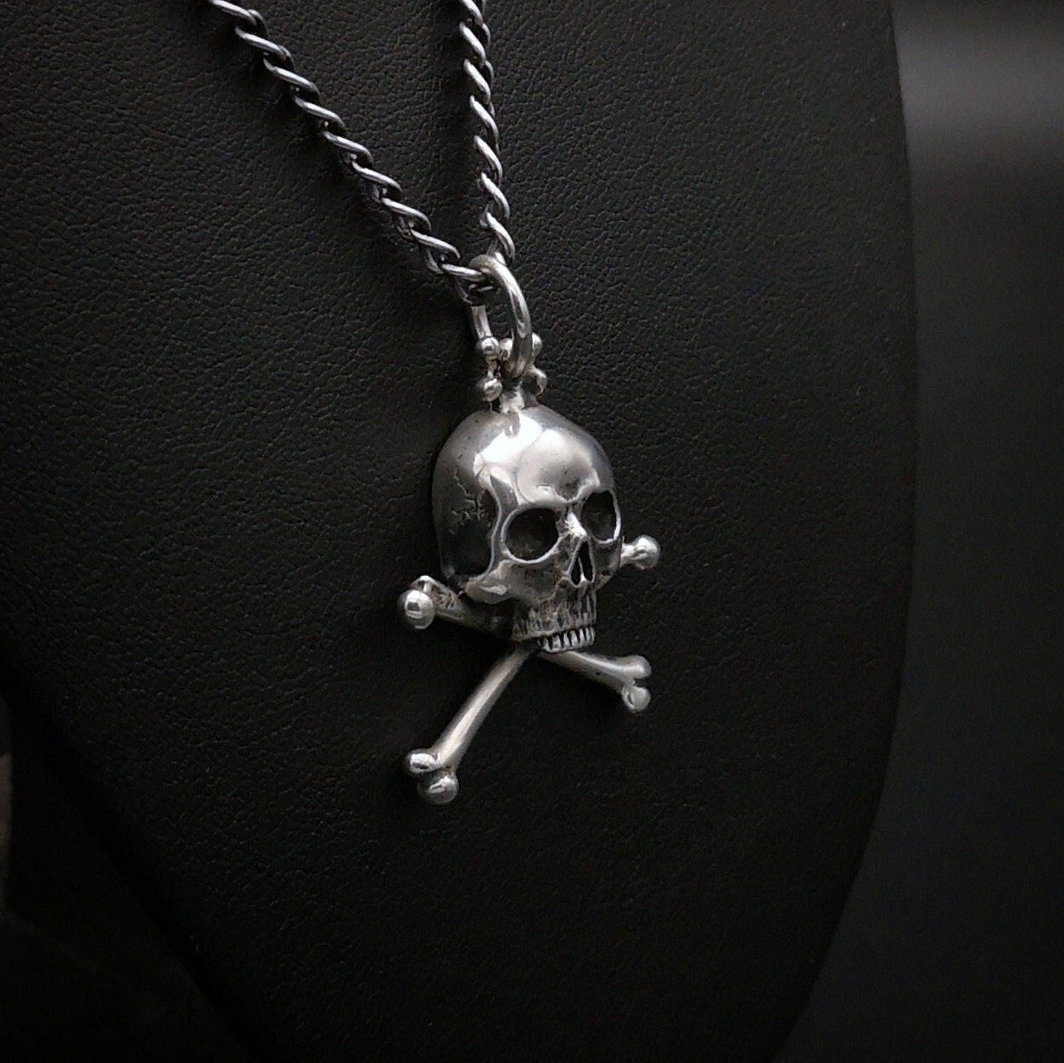 Silver skull and crossbones pendant on a chain against a dark background
