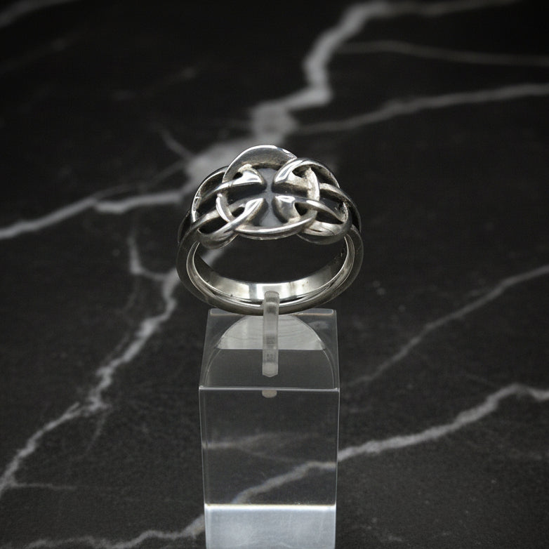 Silver Celtic knot ring on a clear stand with a dark marble background