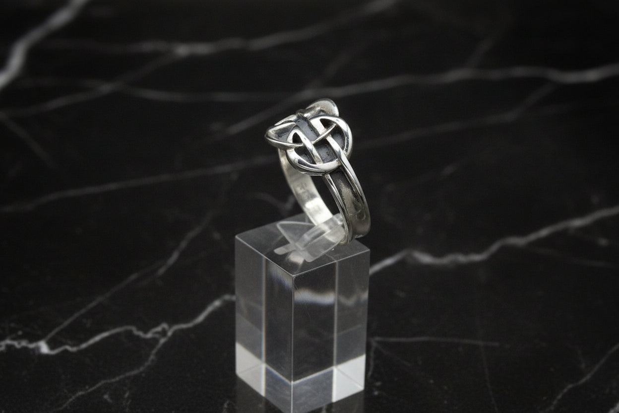 Silver ring with a knot design on a clear stand against a black background