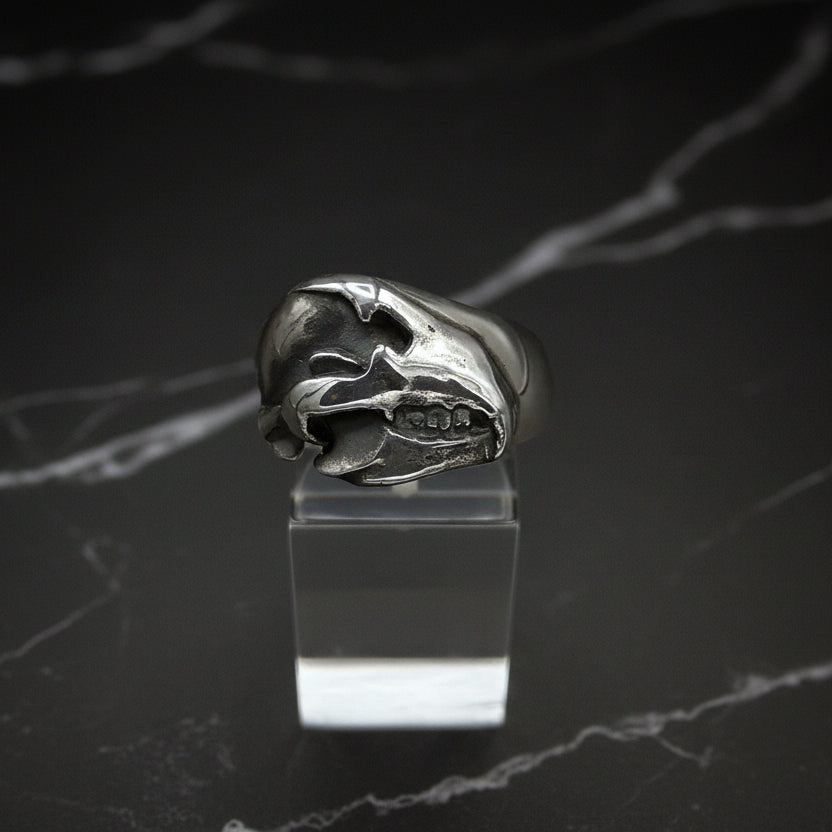 A sterling silver bear skull ring placed on a clear stand against a black background.