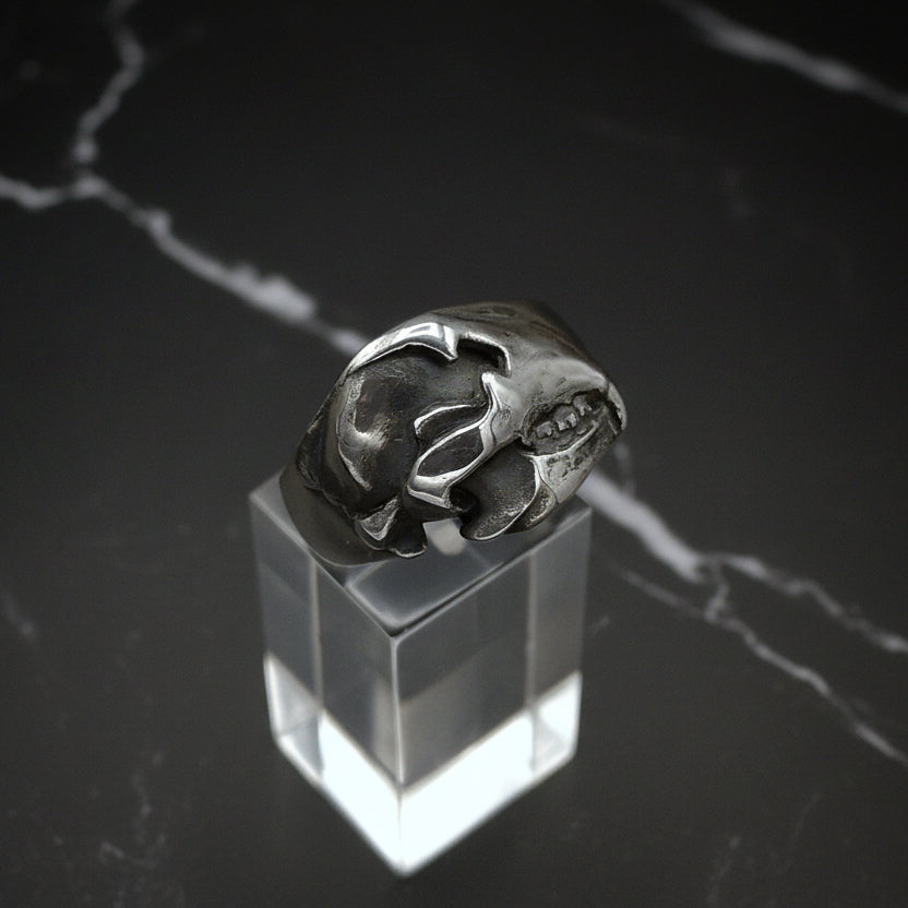 Silver bear skull ring on a clear stand with a dark marble background