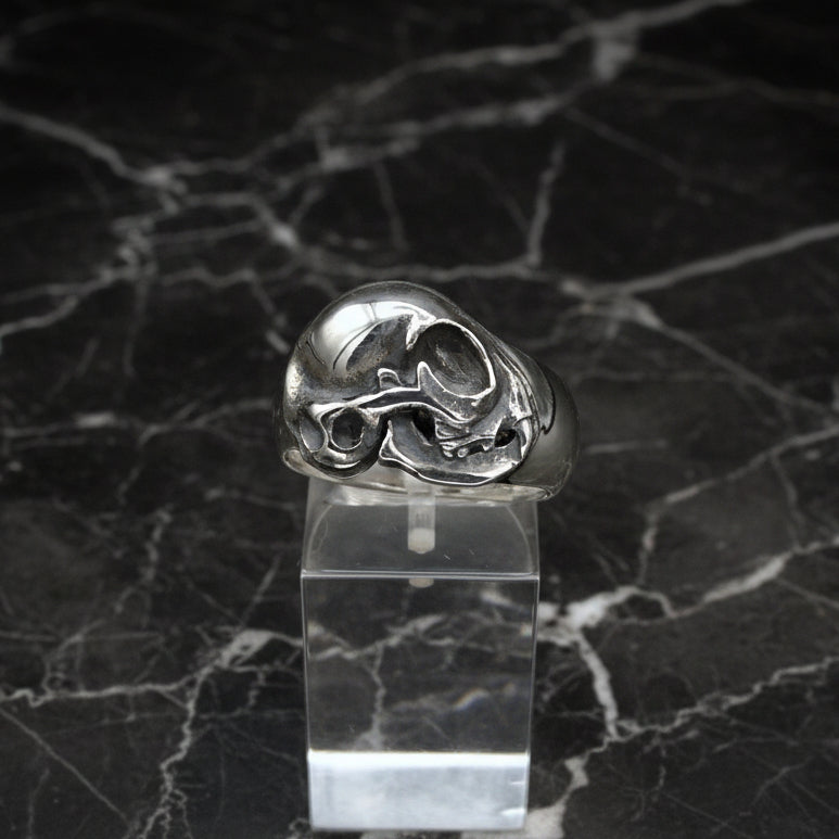 A sterling silver cat skull ring displayed on a clear stand against a dark background.