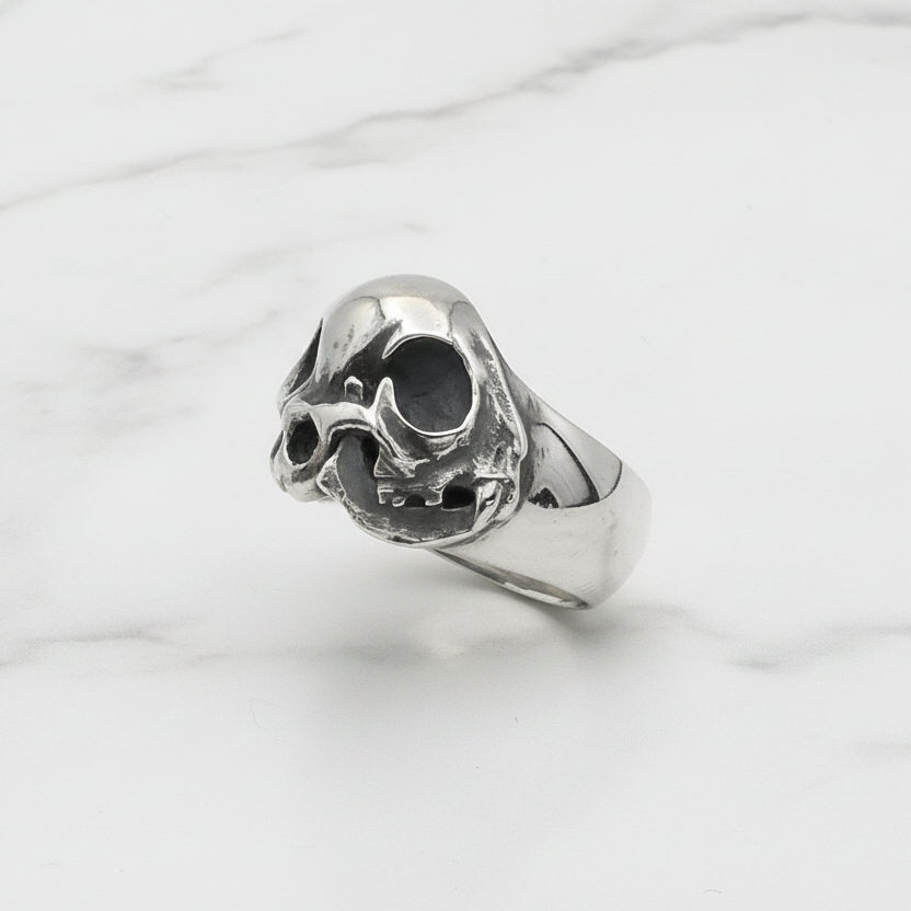 Silver skull-shaped ring on a clear stand against a white background