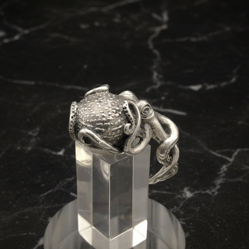 Silver octopus ring on a clear stand against a dark marble background