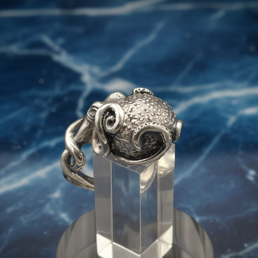 Silver octopus ring on a clear stand against a blue marble background