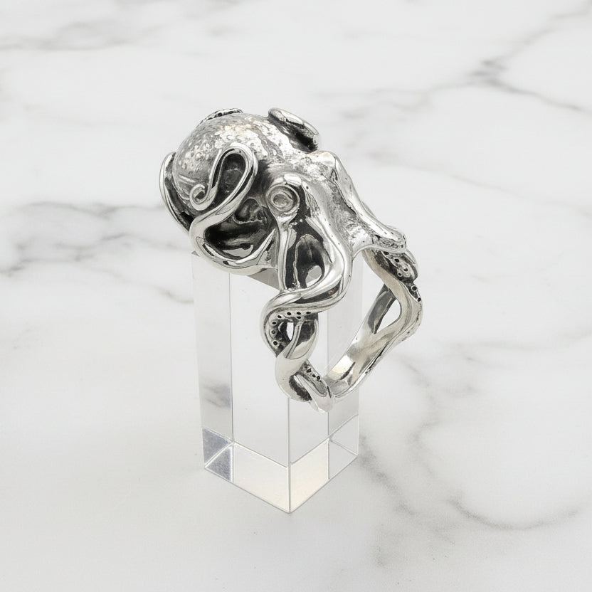 Silver octopus ring with intricate design on a clear stand against a white background