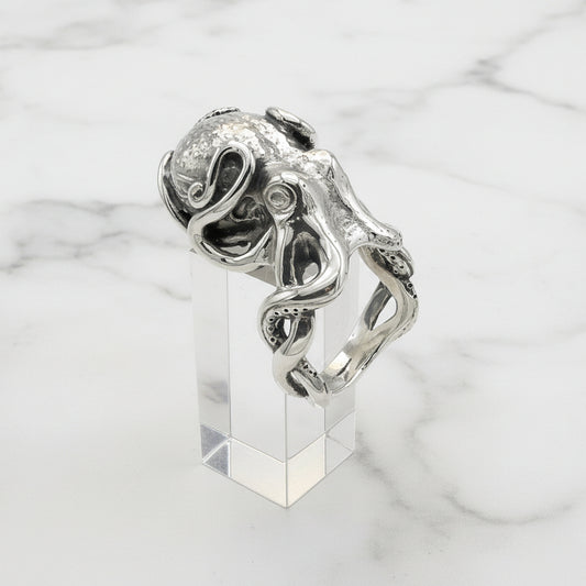 Silver octopus ring with intricate design on a clear stand against a white background