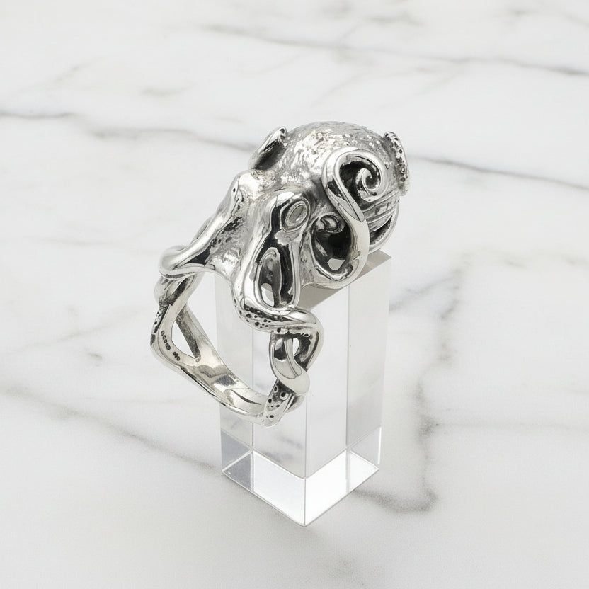 Silver octopus ring with intricate design on a clear stand against a light gray background