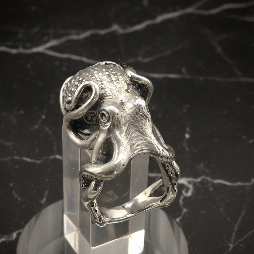 Silver octopus ring on a clear stand against a dark background