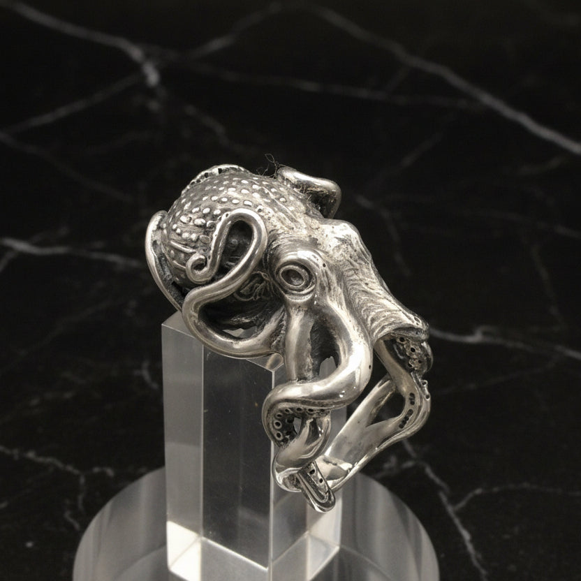 A large silver octopus ring displayed on a clear stand, with a polished finish.
