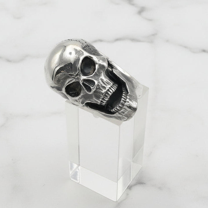 Silver skull ring on a clear stand against a white background