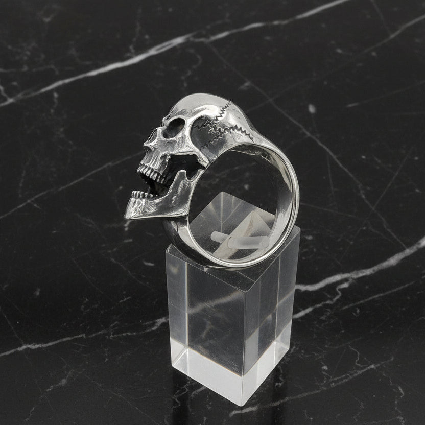 Silver skull ring on a clear stand against a white background