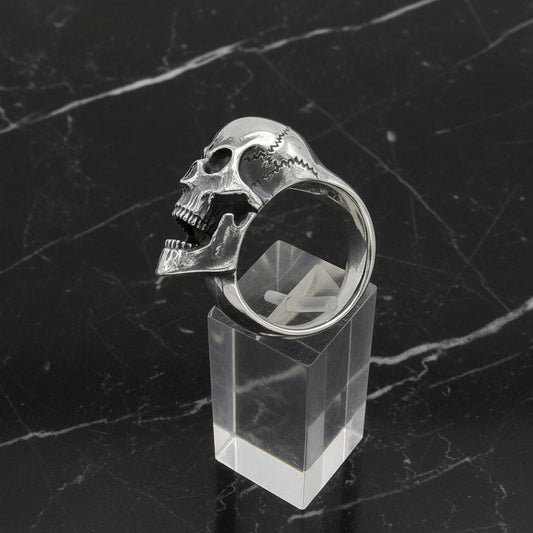Silver skull ring on a clear stand against a white background