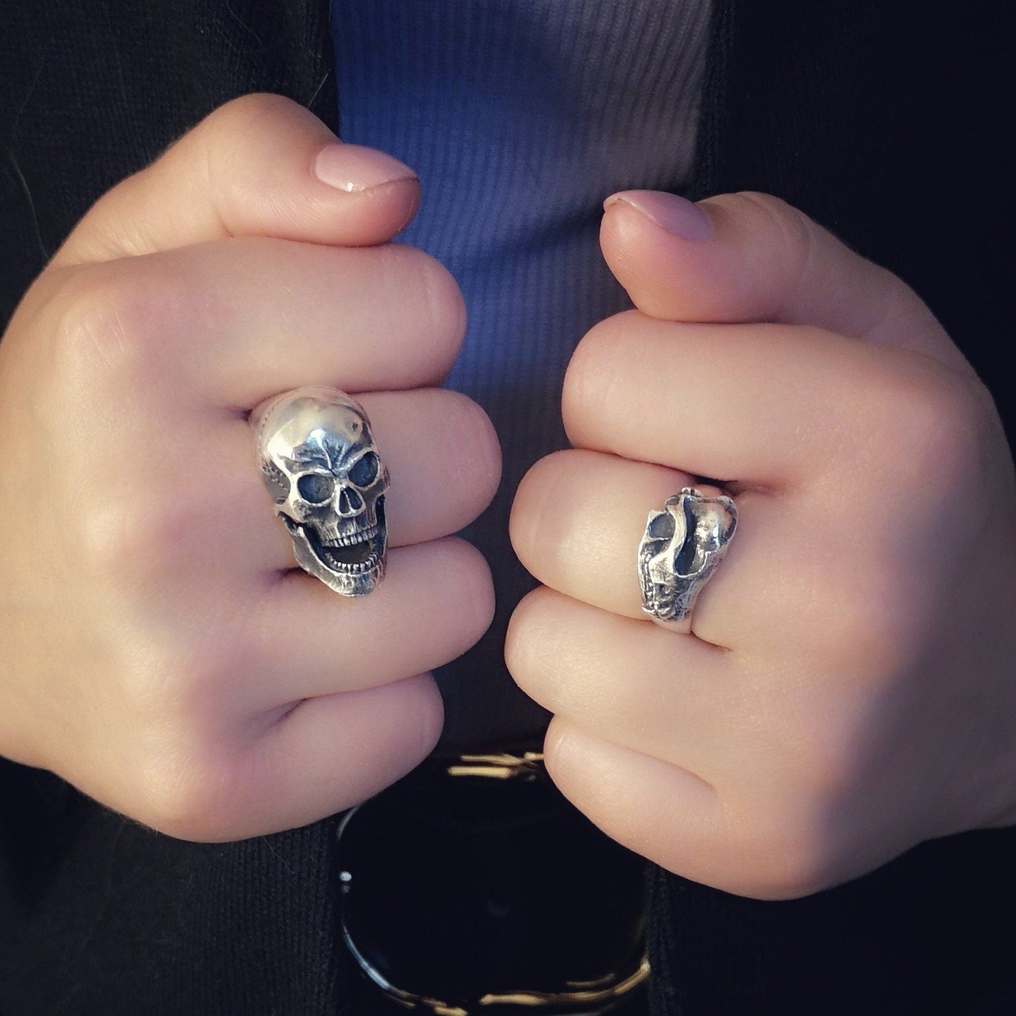 Close-up of hands wearing skull-themed rings with a blurred background