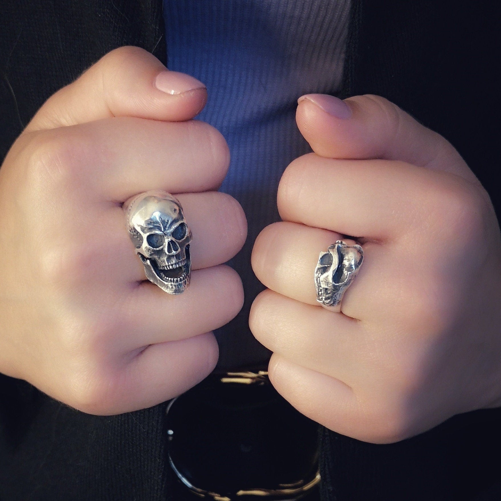 Close-up of hands wearing skull-themed rings with a blurred background